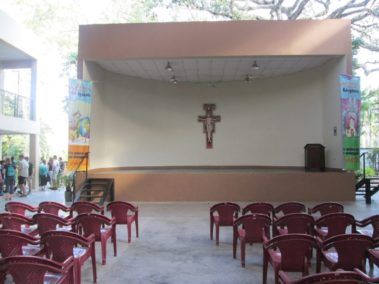 Empty seats in front of a stage with a podium and a crucifix