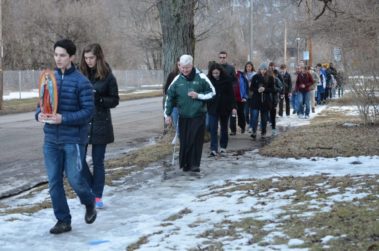 Large group of students following a student with a statue of Mary