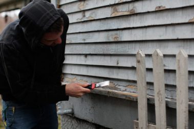 Student removing paint chips from the siding of a home
