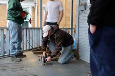 Student sawing the deck of a home