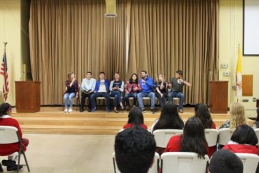 Students sitting in chairs in a line on a stage