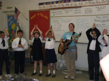 Student playing guitar while children follow along with a dance