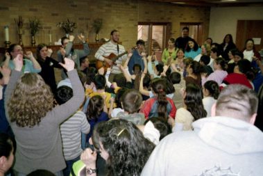 Students and children listening to a man playing guitar