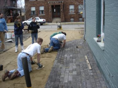 Students laying stones in the ground alongside a building